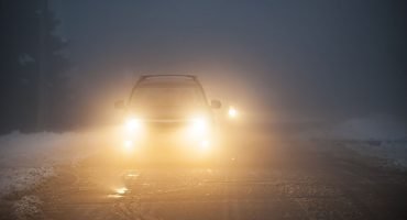 Bright headlights of a car driving on foggy winter road